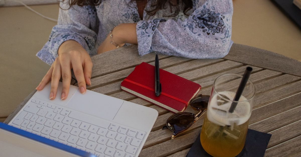 Laptop and notebook on a cafe table with a coffee cup and natural window light